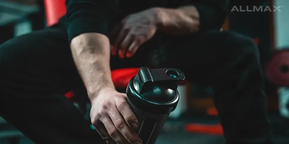 a man holding an ALLMAX shaker cup