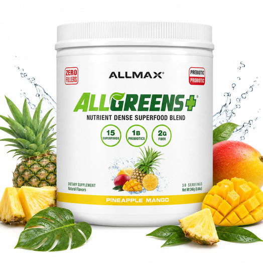 A white tub of ALLMAX AllGreens+ Nutrient Dense Superfood Blend dietary supplement, surrounded by fresh pineapple, mango, and green leaves on a white background with water splash graphics.