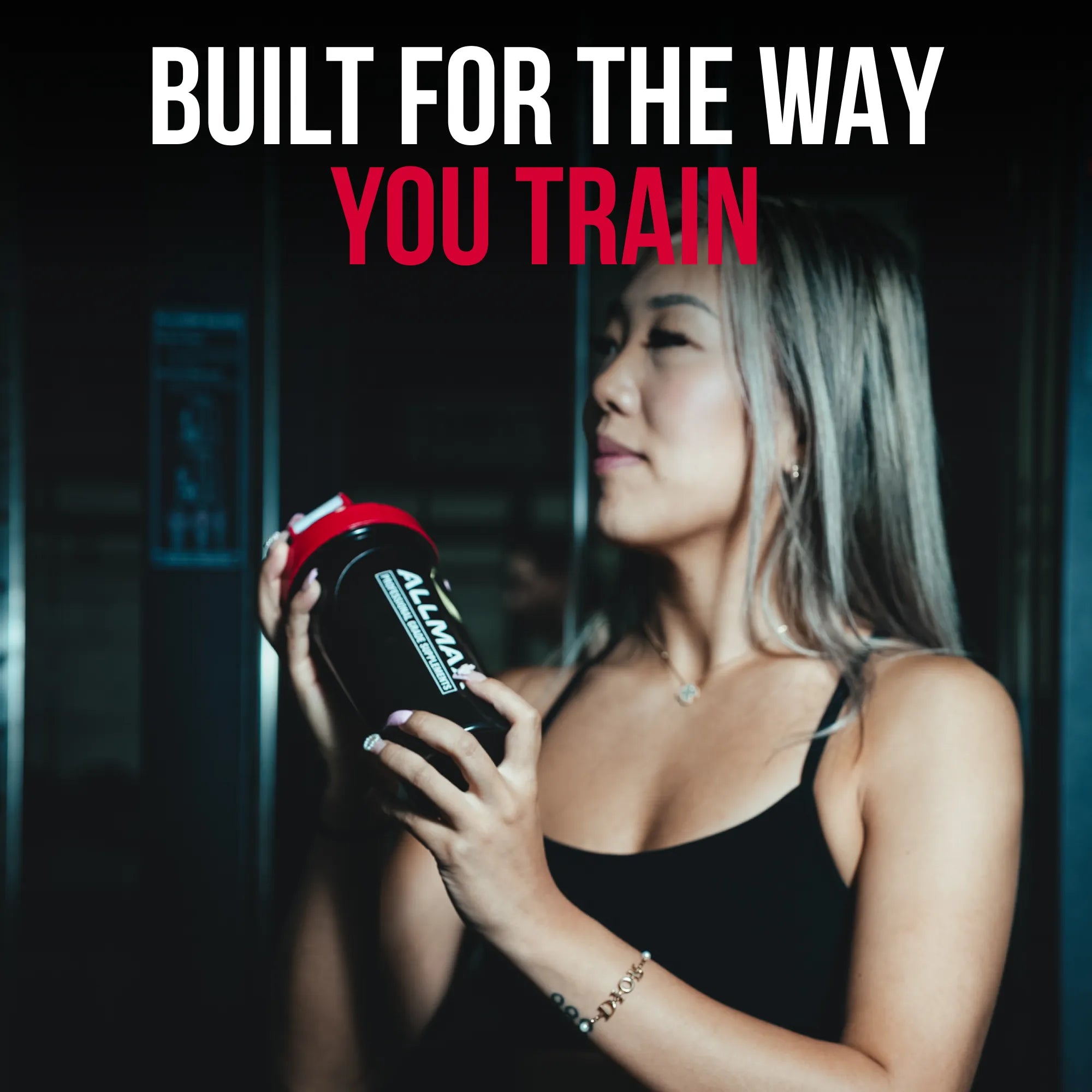 A woman in a black tank top holds a black shaker bottle with a red lid and white text. Large text at the top reads 'BUILT FOR THE WAY YOU TRAIN' in white and red.